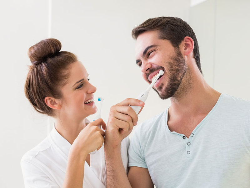 man and woman brushing teeth with electric brushes