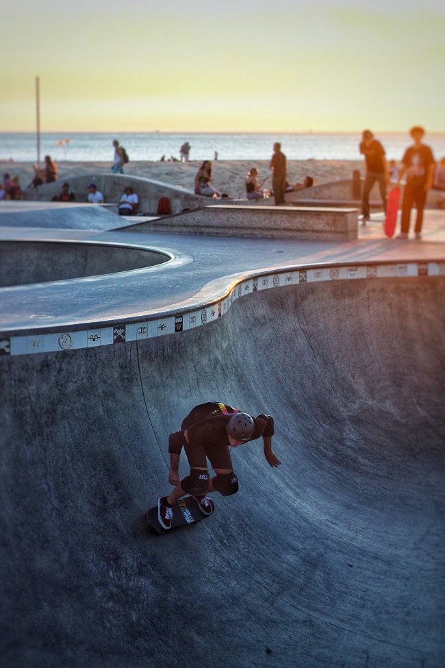 picture of a man doing skateboard tricks in a skateboard park around with other people wearing a knee pads and other protective gear 