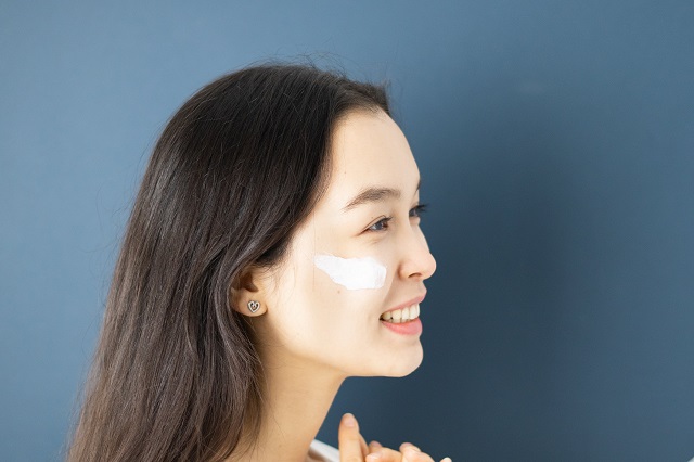 picture of a woman putting a face cream in front a blue background 