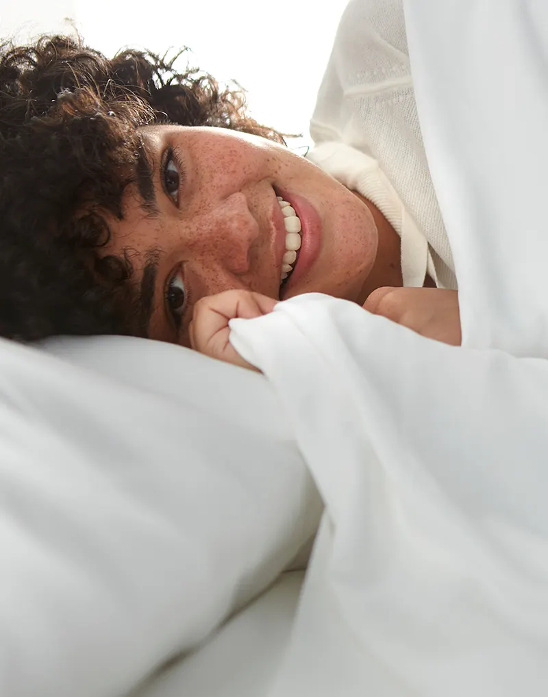 woman in bed looking at the camera holding bamboo bed sheets