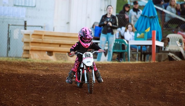 Kid in black and pink motorbike gear driving dirt bike