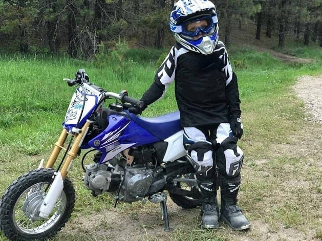 Kid with motorbike gear standing by his motorcycle in nature