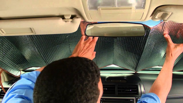 man installing and adjusting car sunshade on his windshield from the inside